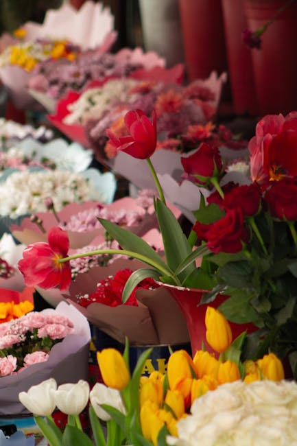A vibrant display of fresh floral bouquets featuring a variety of flowers, including bright red tulips, pink roses, and yellow tulips, arranged together in an indoor flower shop environment. The flowe